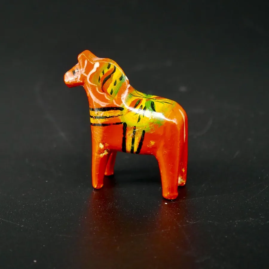 Red wood Dala horse side profile revealing hand-painted geometric patterns on saddle blanket with yellow and black stripes