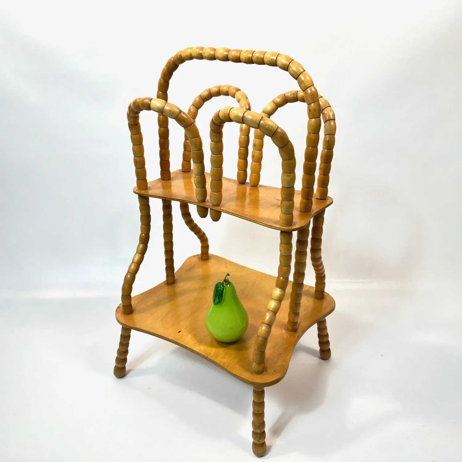 Swedish mid-century wooden magazine rack with rotating beaded frame, two golden-honey timber shelves, and sculptural spindle