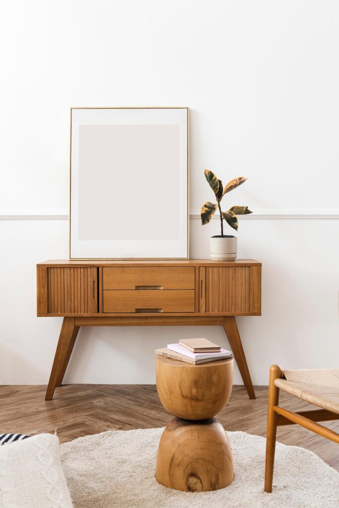 Teak credenza with empty frame, wooden stool, and botanical plant in minimalist entryway setup