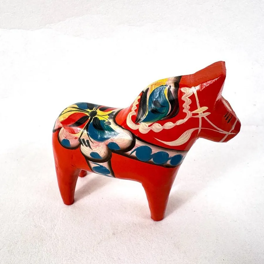 Vintage Dala horse in bright red with painted saddle detail, shot from three-quarter angle against neutral background