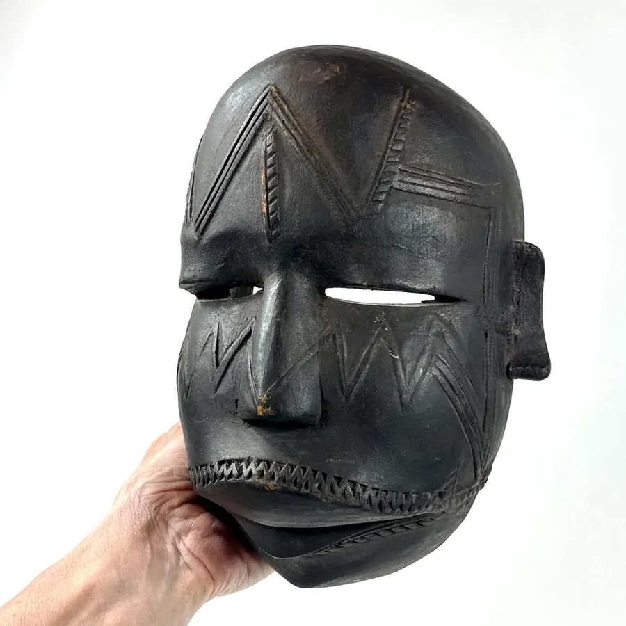 Vintage tribal mask held in hand, carved wood with triangular forehead markings, visible patina and traditional proportions