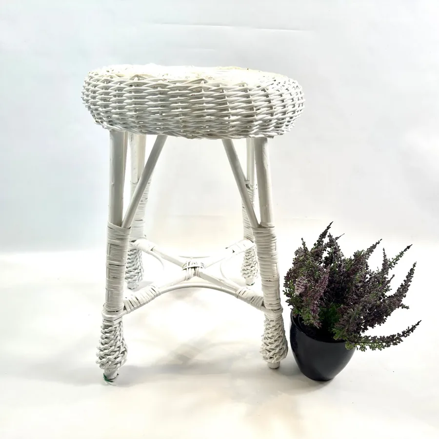 Vintage white rattan stool with woven seat and tapered legs, styled with potted dark plant, three-quarter view