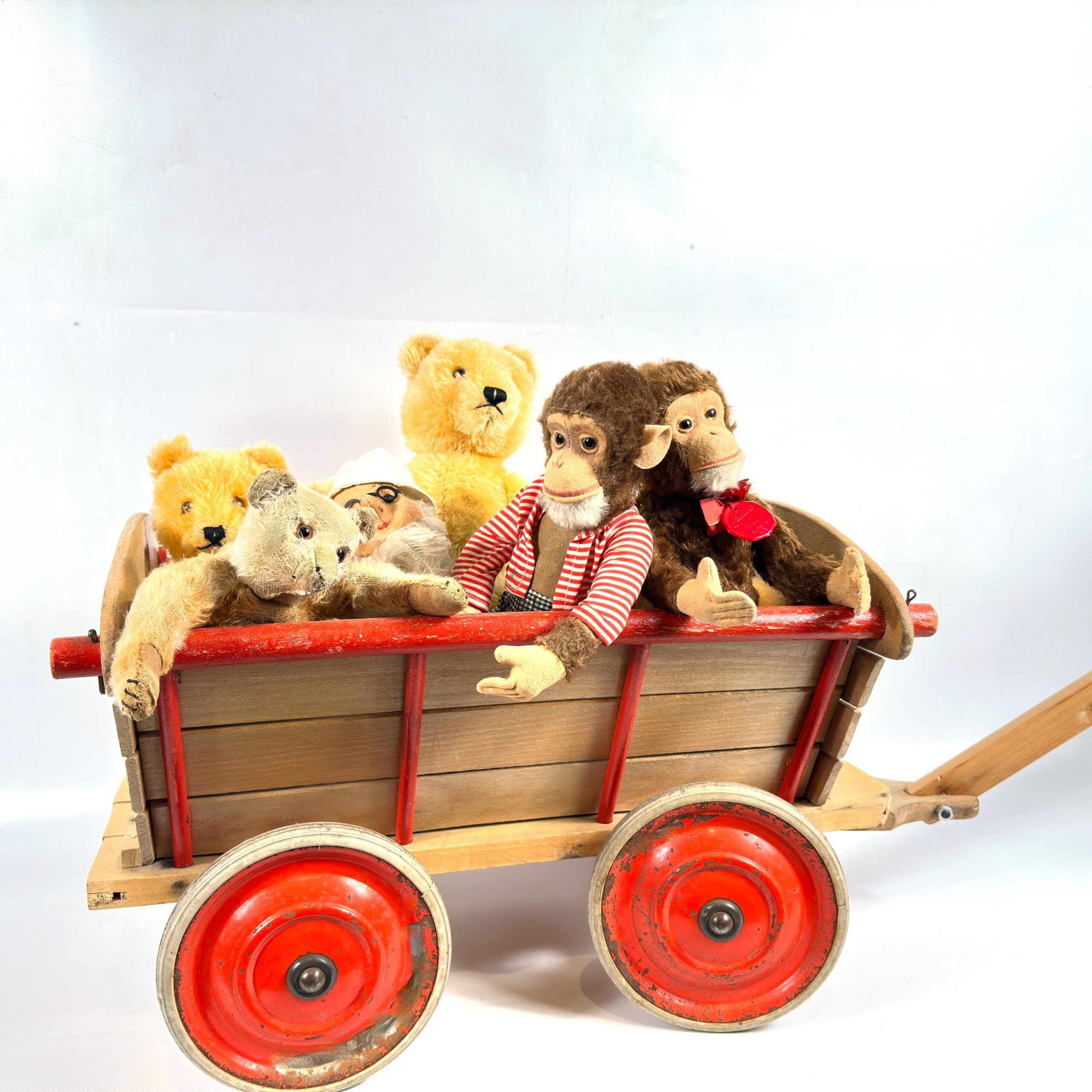 Wagon filled with three teddy bears and dressed doll from elevated angle, showing red wheels and wooden handle in context