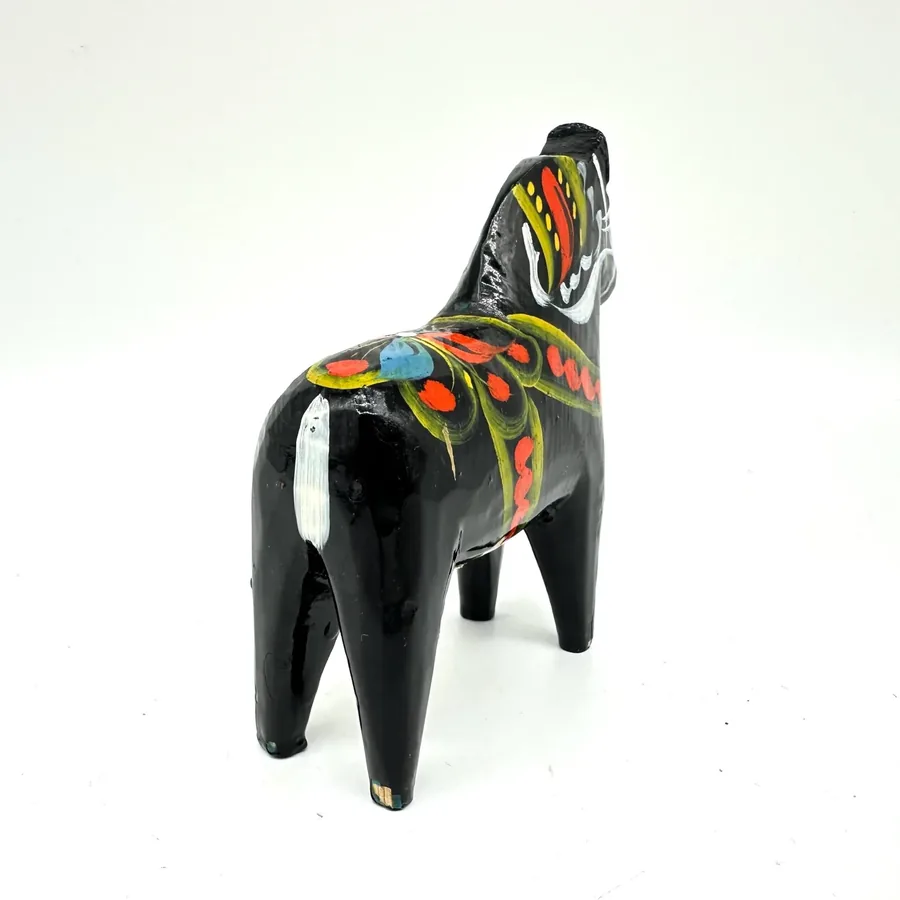 Wooden dala horse with black gloss finish, displaying colorful hand-painted blanket and bridle, captured from angled perspect
