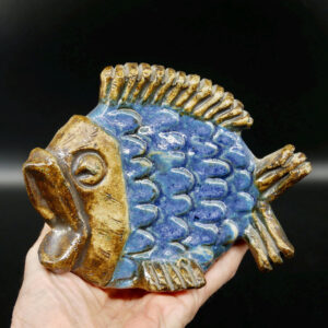 Willy Fischer ceramic fish sculpture, cobalt blue glaze body with golden-brown glazed head and fins, held in hand against dar
