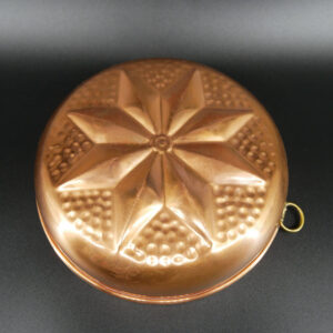 Vintage copper jelly mold with radiating eight-petal design and dotted sections, brass hanging loop visible