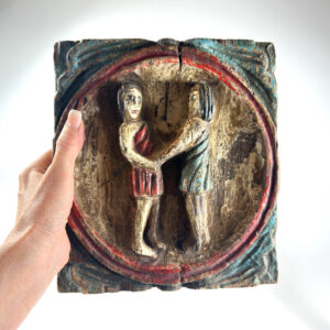 Vintage hand-carved wooden Gemini zodiac panel with twin figures in red and gold circular frame, held in hand