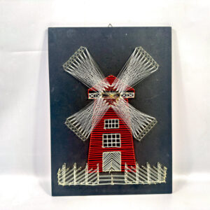 Vintage 1970s string art windmill on black board with red structure, white thread detailing, and brass nail accents