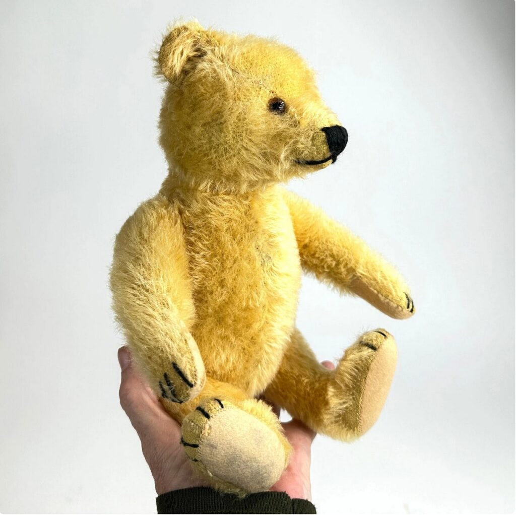 Soft yellow mohair teddy bear held upright, showing pristine condition with bright coloring and well-defined facial features