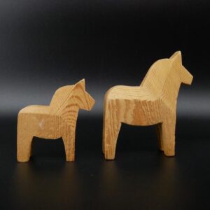 Pair of hand-carved wooden Dala horses in natural wood finish, larger horse with arched neck alongside smaller companion piec