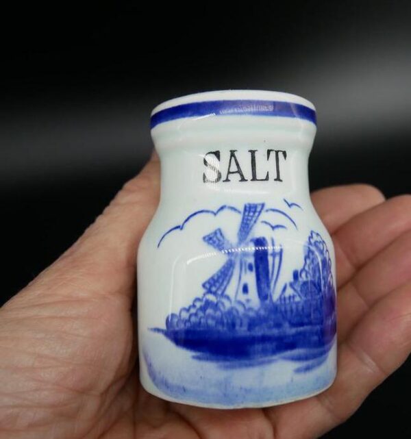 Hand holding cream ceramic salt shaker with blue windmill scene, showing scale and tactile ceramic body warmth