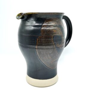 Hand-thrown studio pottery pitcher in dark brown stoneware with expressive swirling glaze, cream base, black handle, artist-s
