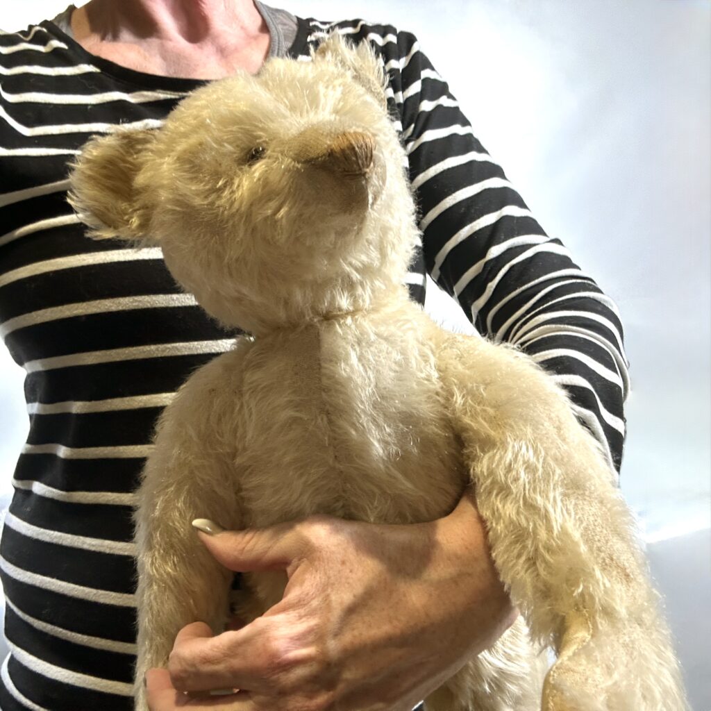 Cream-colored vintage teddy bear held in hands against striped clothing, showing soft mohair texture and crafted details