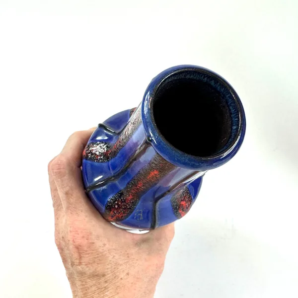 Angled hand-held view showing vase opening, molten glaze flow, red-black textured surface, and shoulder sculptural form