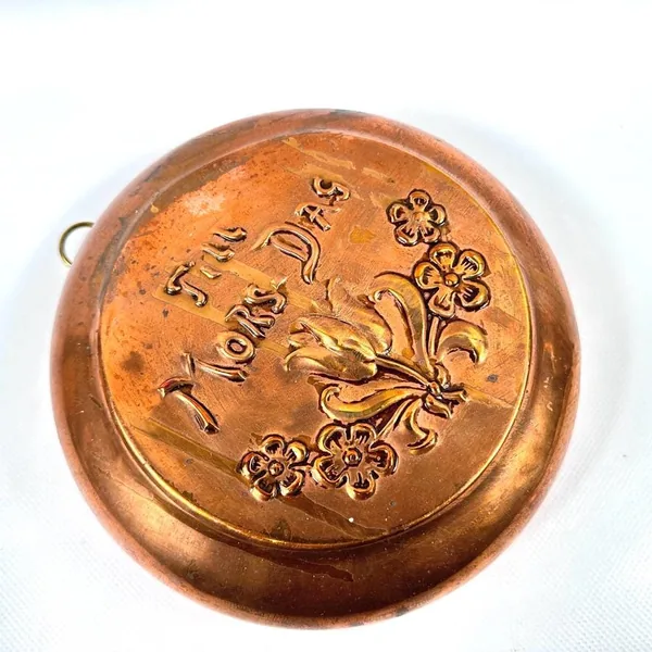 Angled photograph of copper plate showing depth of embossed text and botanical relief against warm surface