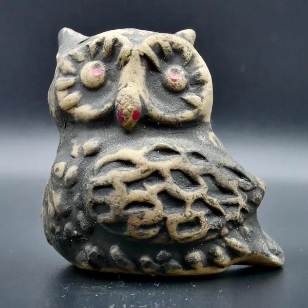 Angled three-quarter view of cream pottery owl with carved linear feather patterns on body and visible artist signature