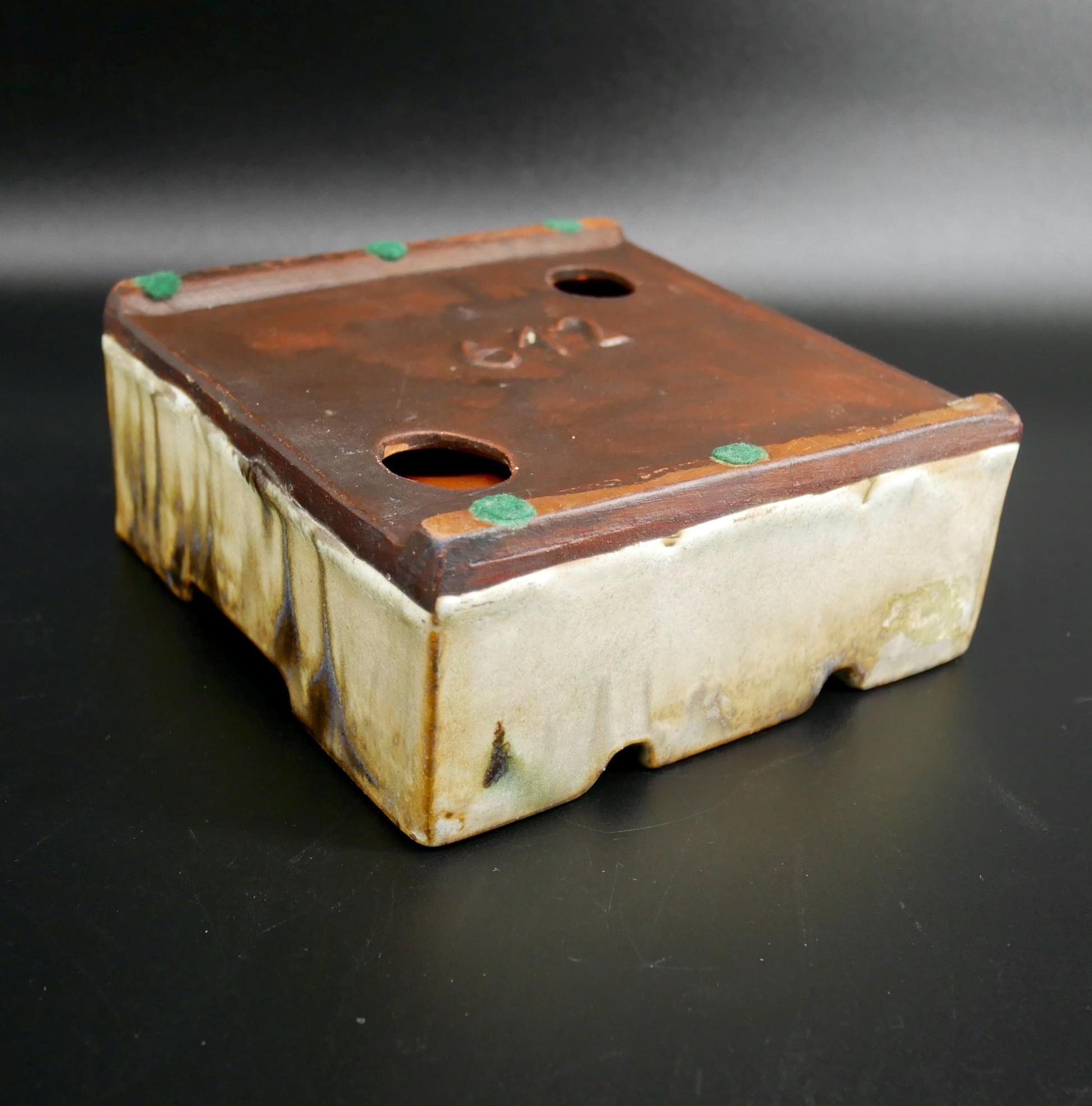 Ceramic ashtray base showing copper or wooden insert plate with two round holes, patina aged surface, vintage hardware detail
