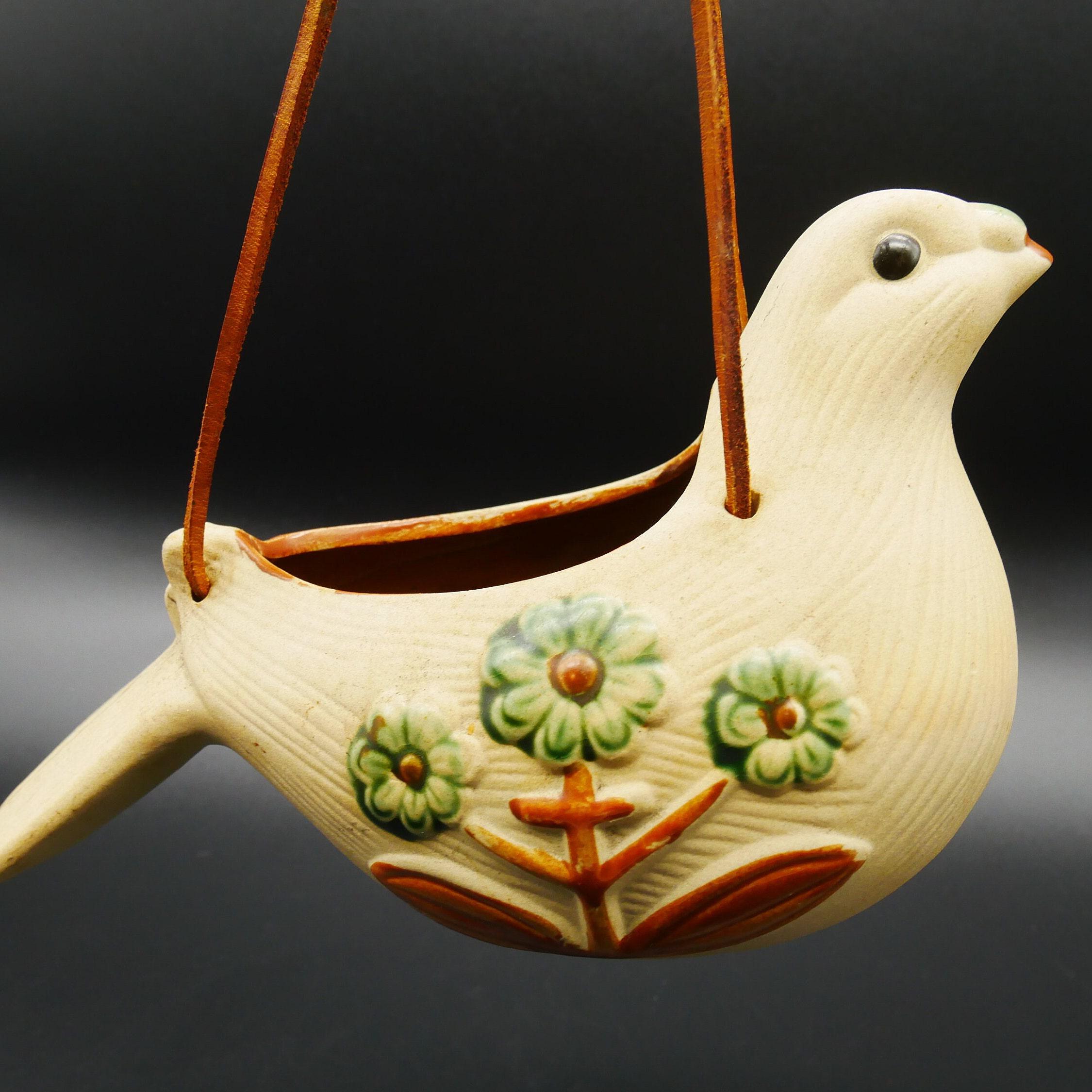 Ceramic bird planter with beige glaze, green raised flowers, and leather hanging cord, front three-quarter view