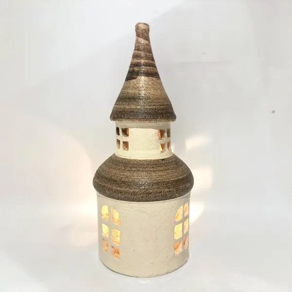 Ceramic tower with glowing yellow light inside windows, striped brown roof, textured stoneware body with cream glaze, lit int