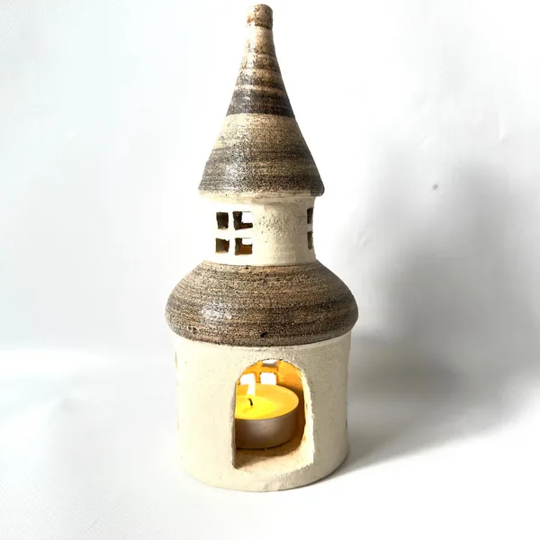 Ceramic tower with open doorway at base, glowing candlelight inside, cream stoneware walls with window openings above entranc