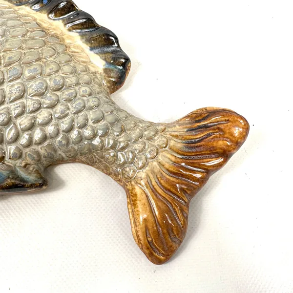 Close-up detail of golden ceramic fish tail fin showing hand-painted glaze work and texture
