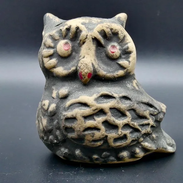Close-up front view of ceramic owl showing dark-painted eyes with pink pupils and rust-toned beak against cream-colored clay