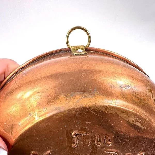 Close-up of copper plate's hanging loop and edge rim detail, showing attachment hardware and metalwork finish