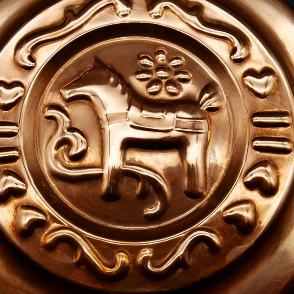 Close-up of embossed Dala Horse and decorative flourishes on copper surface