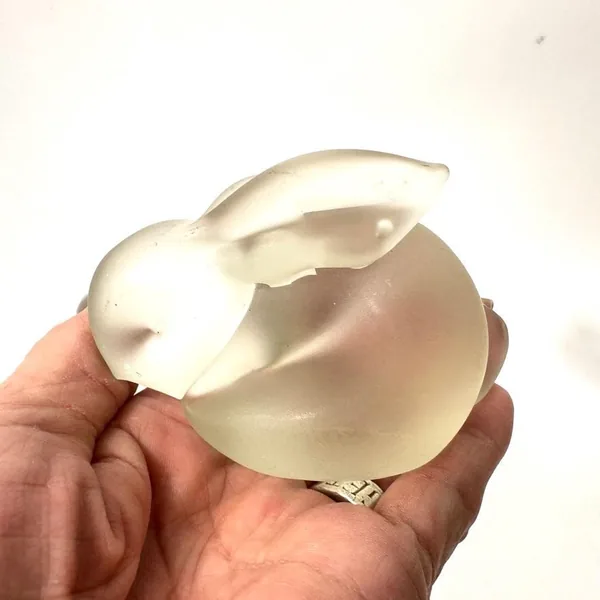 Close-up of frosted glass rabbit held in fingers, emphasizing ear definition, smooth body curves, and pale satin finish quali