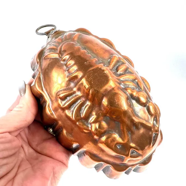 Copper lobster mold cradled in hand displaying full form with warm golden-bronze patina