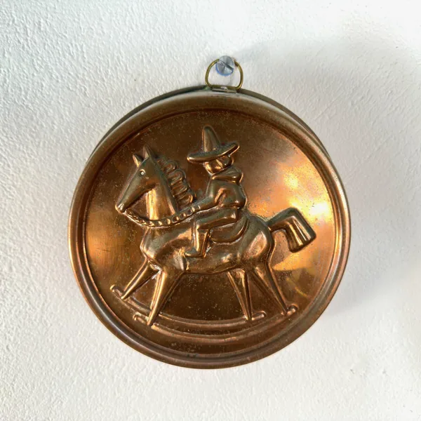 Copper mold lit from side showing dimensional embossed folk art horse with rider, brass loop visible at top