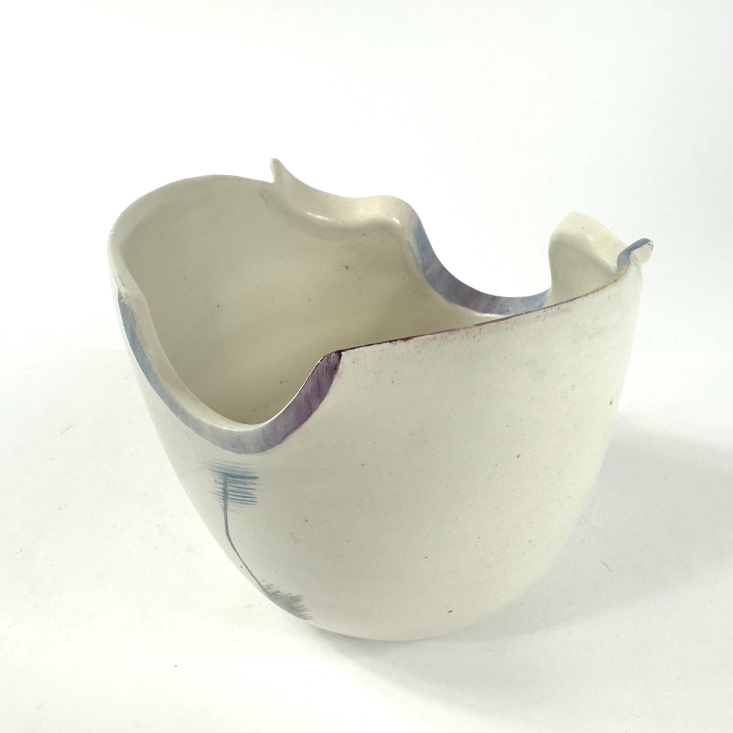 Cream stoneware pottery bowl displaying sculptural rim edges, abstract brushstrokes in blue and purple tones, three-quarter v