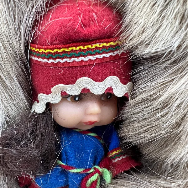 Extreme close-up of doll's rubber face with rosy cheeks and painted features framed by red embroidered woolen hat