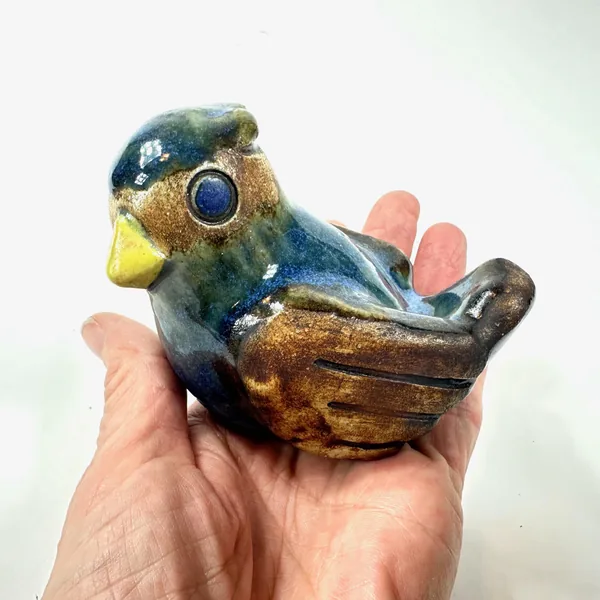 Fischer ceramic bird in hand showing full sculptural profile, glaze patina and hand-painted details across body and wings