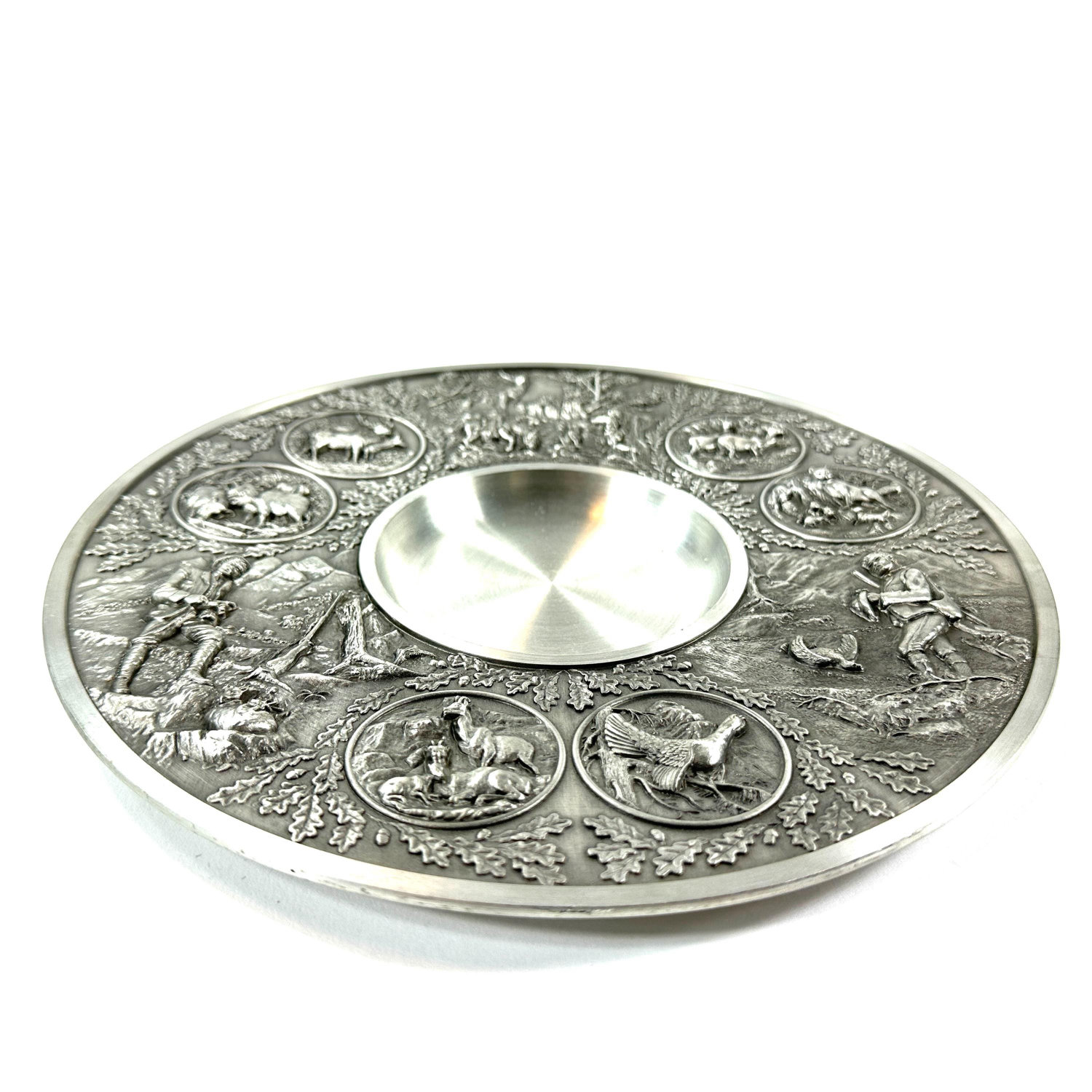 Flat lay of pewter wall plate at slight angle, showing dimensional relief depth and metal texture across entire surface