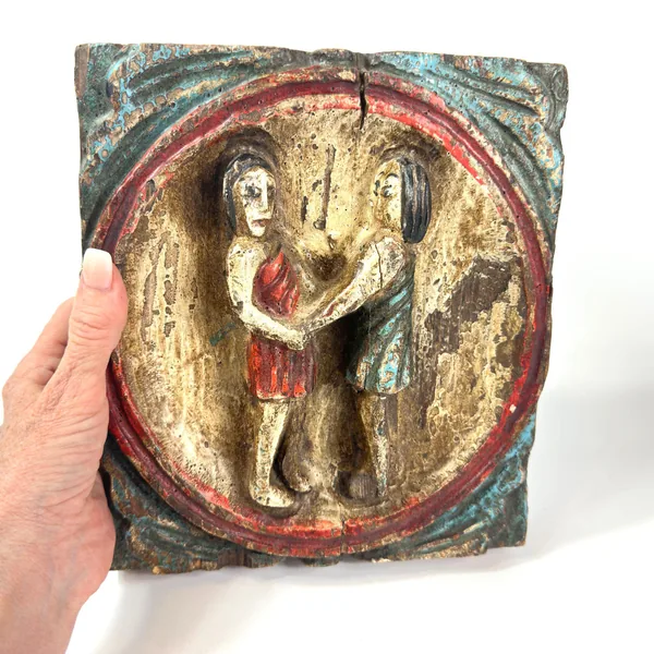 Hand-held close view of carved Gemini zodiac wood art emphasizing fine carving details and paint texture