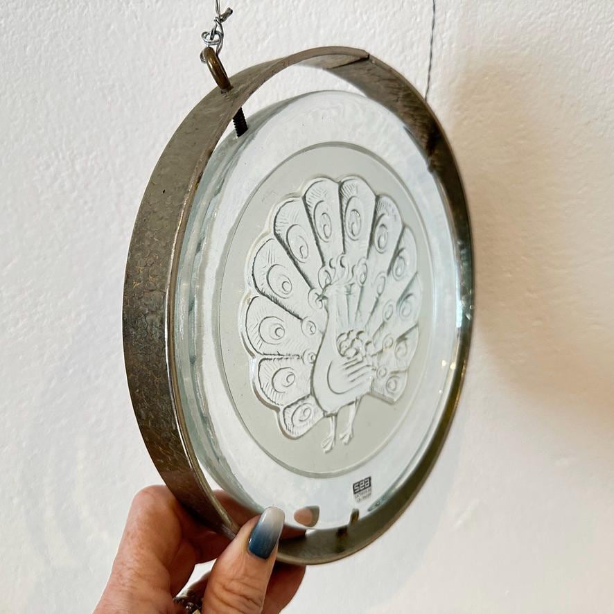 Hand-held peacock glass panel with clear focus on feather detailing and the bird's confident profile in pressed relief