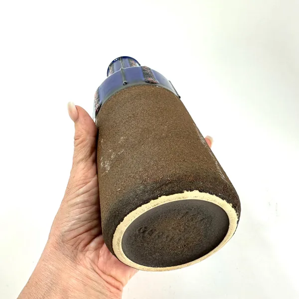 Hand-held side view of vase base and lower body showing unglazed stoneware texture, cream rim, form number, and cylindrical f