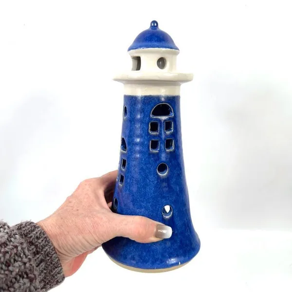 Hand holding blue ceramic lighthouse showing scale, 24cm height, textured glaze, and weight of vintage pottery piece