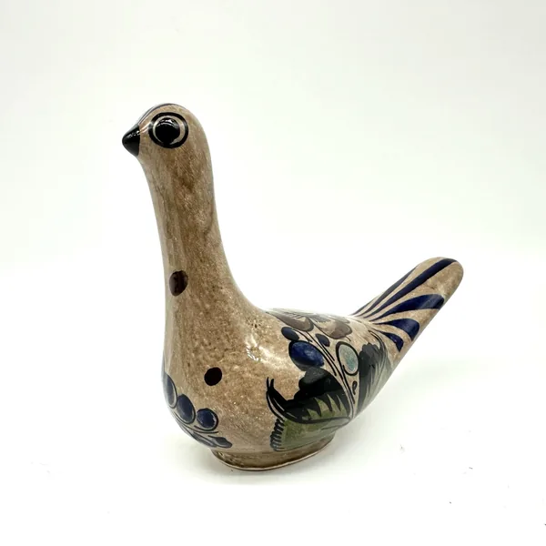 Hand-painted Mexican bird sculpture, side-front view showing green wing feathers, dark foliage, and blue striped tail detail