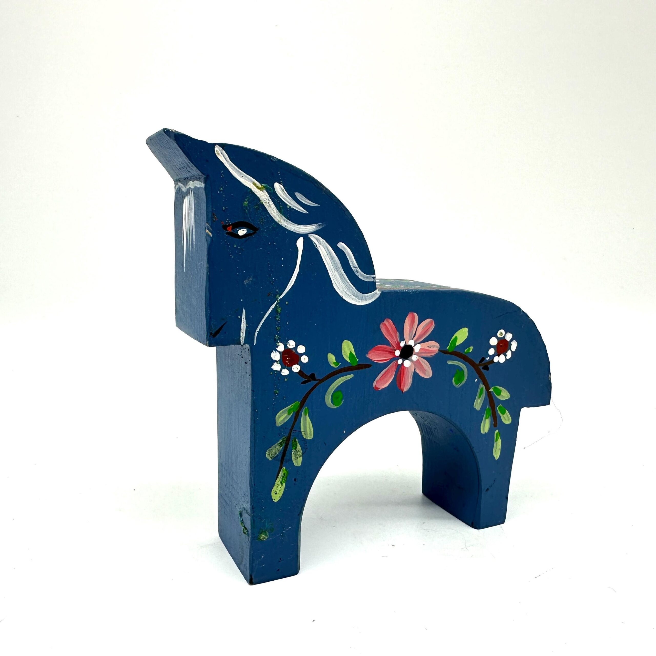 Hand-painted Swedish Dala horse in deep blue wood with pink floral motifs and green leaf details, front three-quarter view