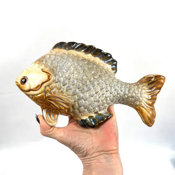 Hand presenting ceramic fish plaque showing full front view with all glazed colors and dimensions visible