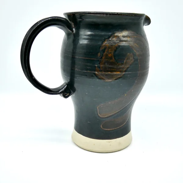 Hand-thrown pottery pitcher showing curved body, sturdy black handle, and expressively glazed decoration in warm brown tones