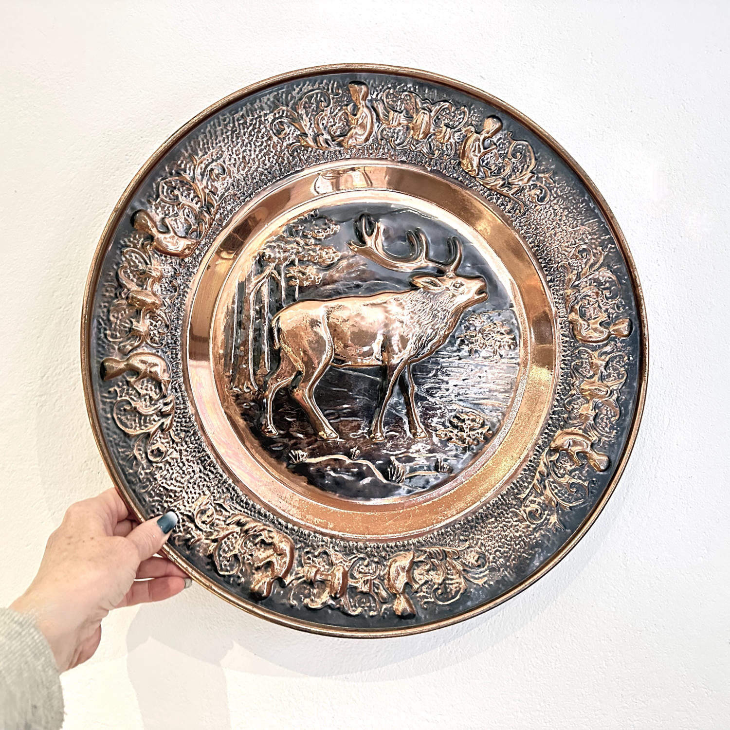 Handheld presentation of full copper stag wall plate showing scale and weight, complete ornamental border visible