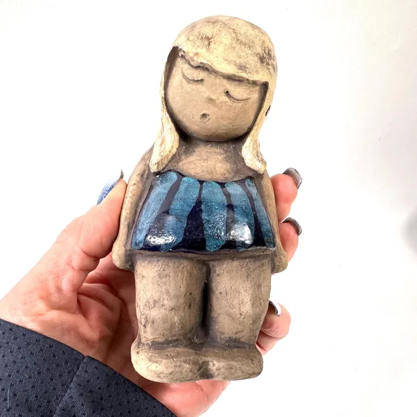 Held in hand showing scale and size, ceramic girl 14 cm tall, blue dress glaze detail, weight and tactile quality visible