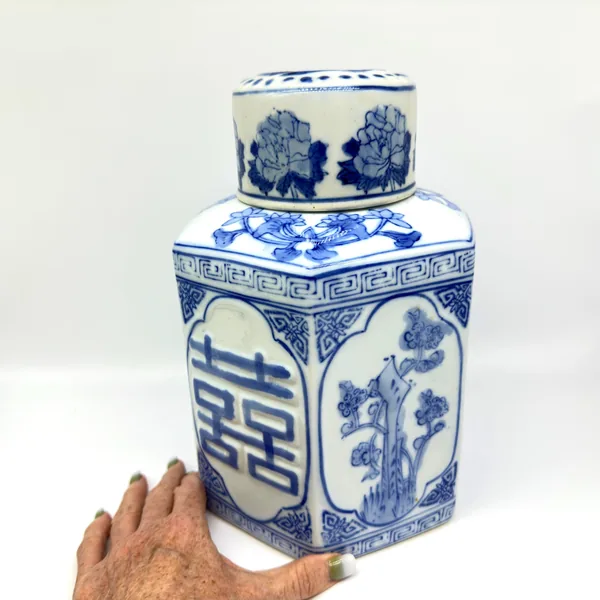 Held porcelain jar detail showing full body design with blue motifs, hexagonal sides, domed top