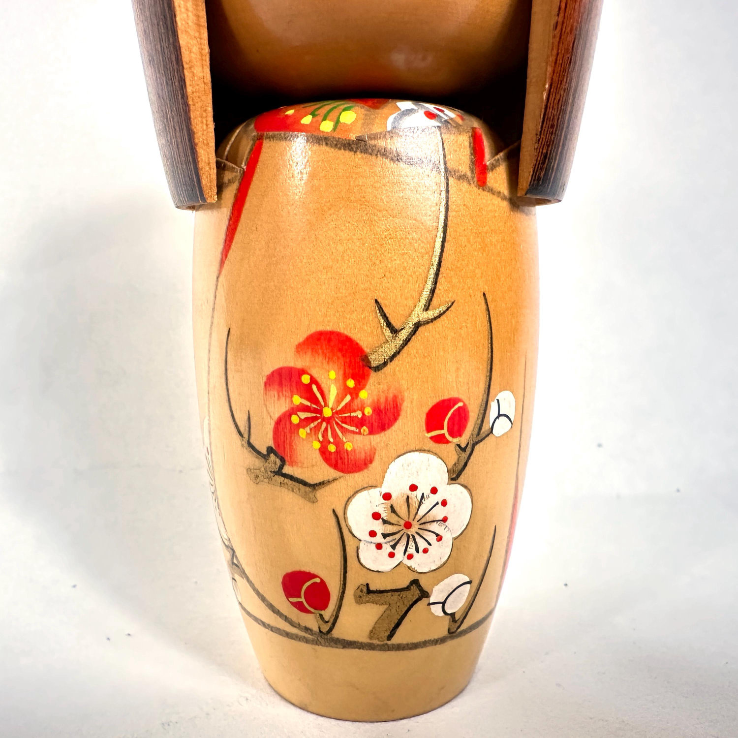 Kokeshi doll closeup of painted decoration, showing red and white flowers with stems and leaves on warm wooden surface