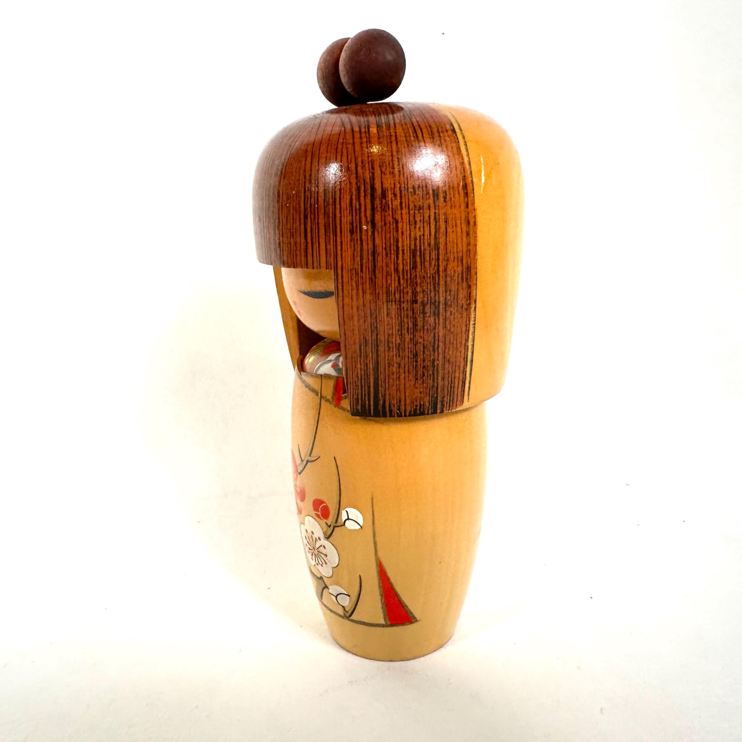 Kokeshi doll side profile angle, showing the cylindrical wooden form with dark head and cream-colored painted body section