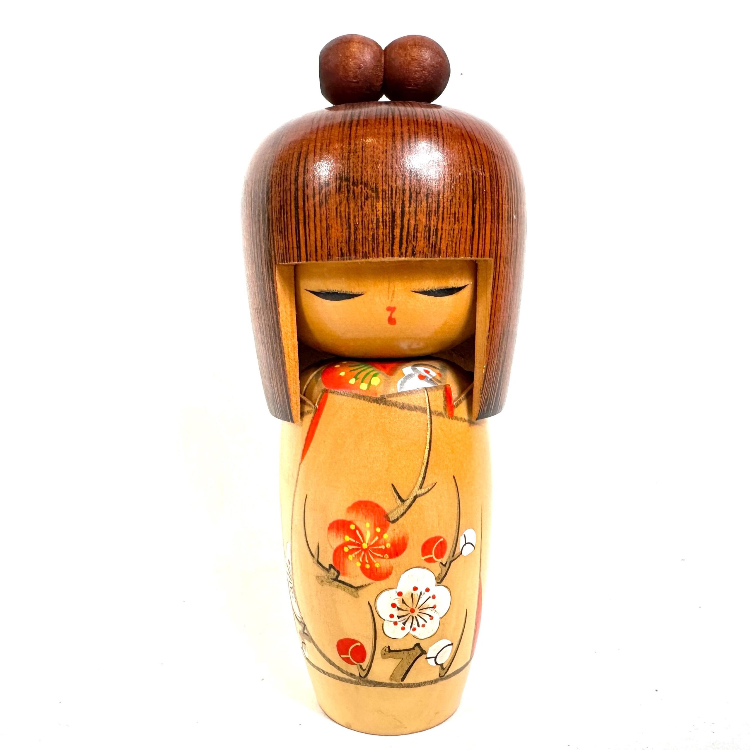 Kokeshi doll standing upright, dark wooden head with two ball knobs, pale yellow body with hand-painted red flowers