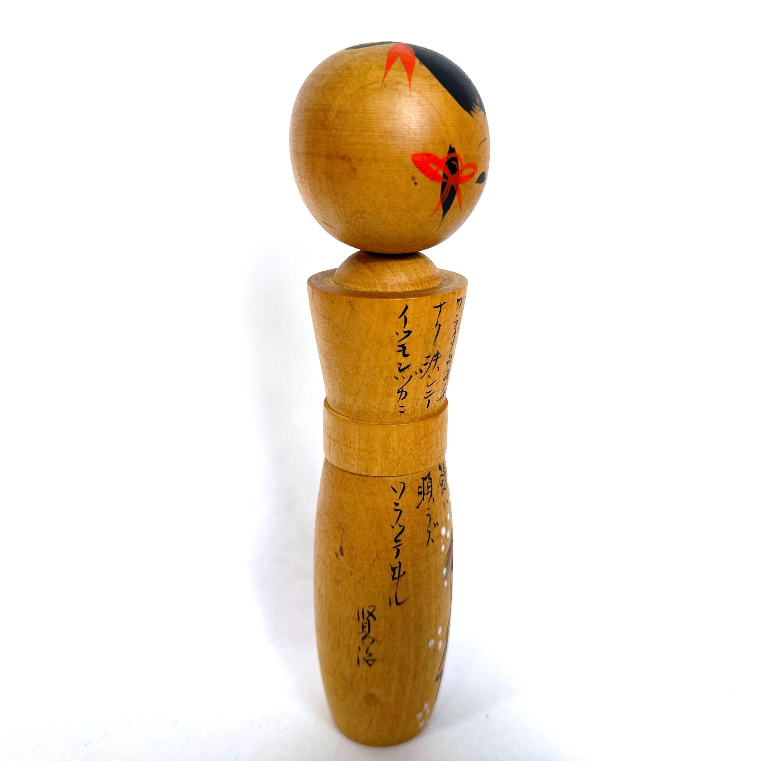 Kokeshi doll with painted head featuring red accent marks and decorated wooden body with calligraphic imagery